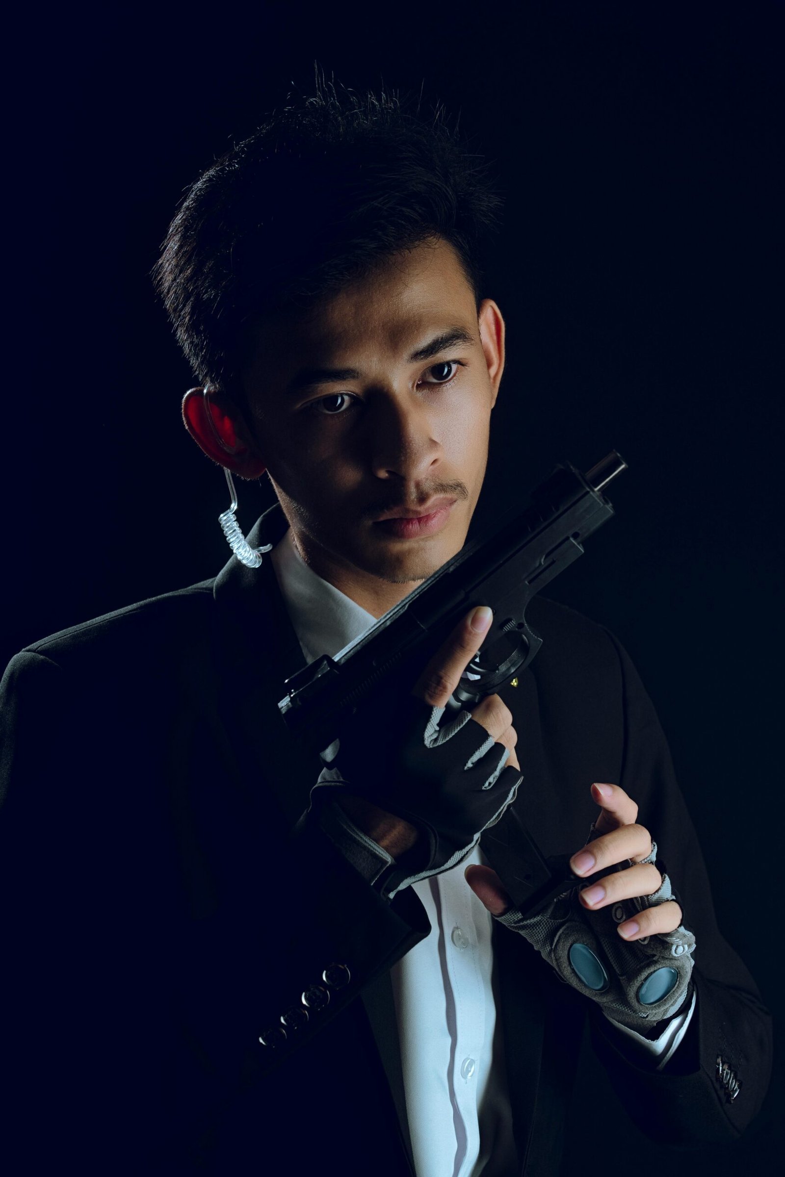 Studio shot of a man in a suit holding a gun, exuding a mysterious, mafia-style presence.