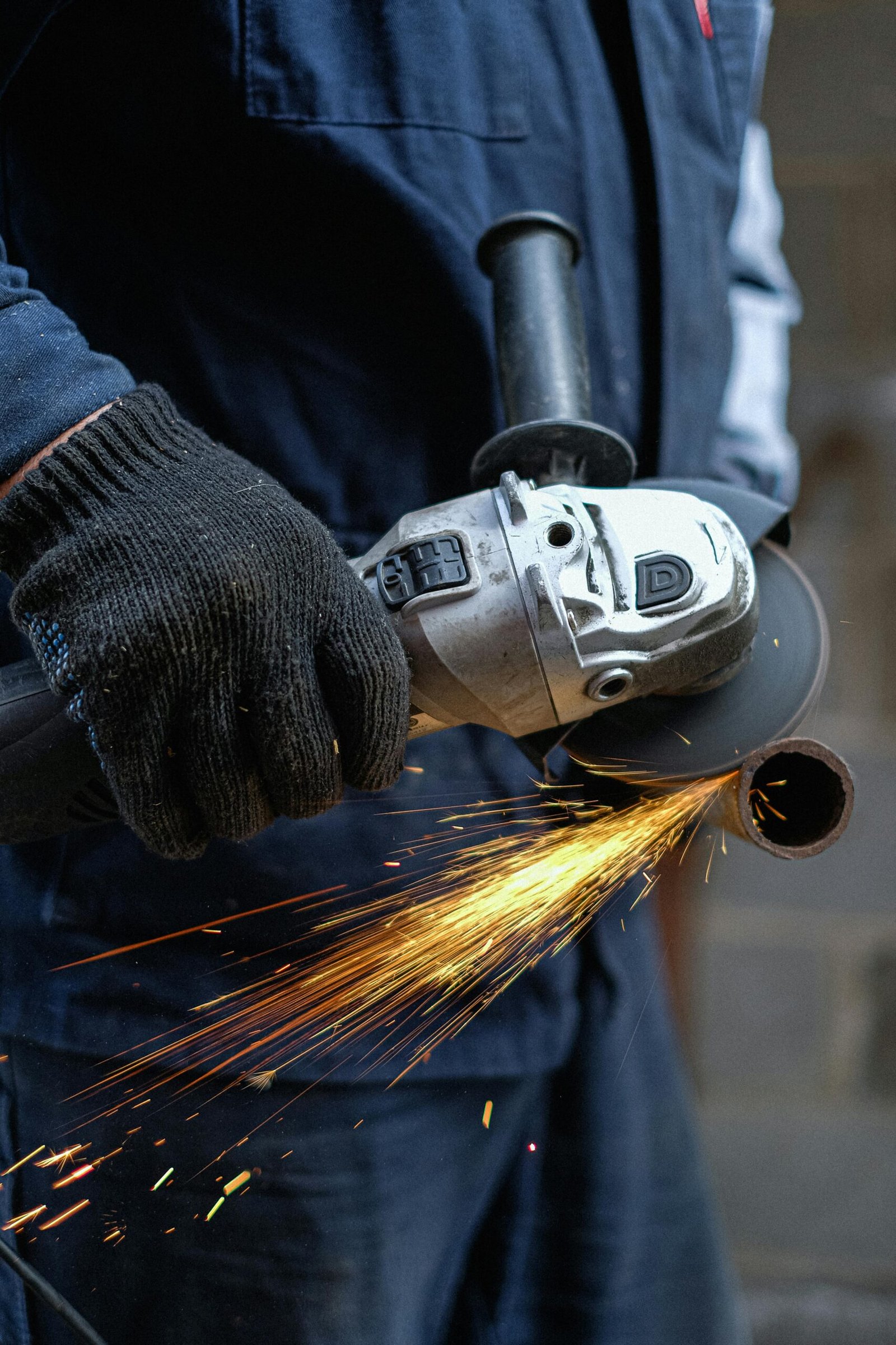 Close-up view of a man using an angle grinder, creating sparks while cutting metal in an indoor workshop.